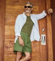 Hombre con bermudas verdes y camisa verde apoyado en una puerta, con una mirada relajada y desenfadada.